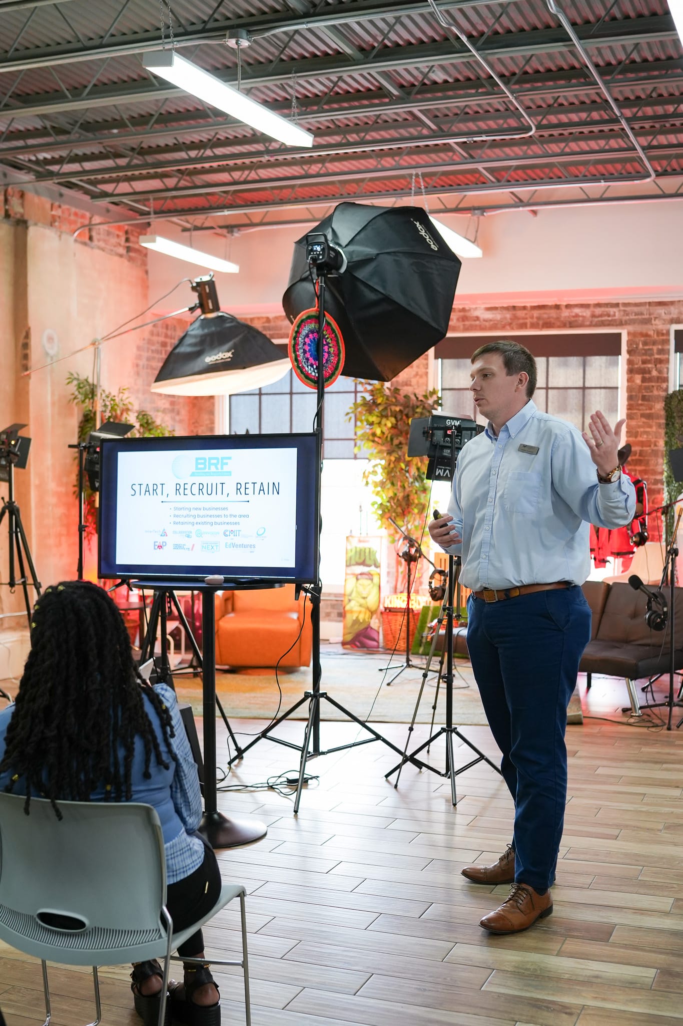 A man giving a presentation titled 'Start, Recruit, Retain' in a studio setting.