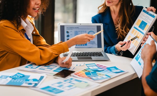 Group of people discussing design layouts and data charts at a table with a laptop.