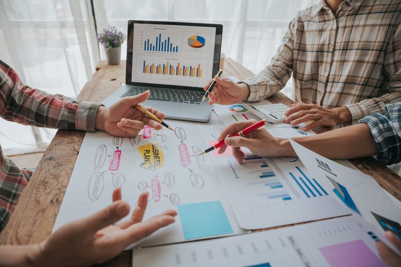 People discussing and pointing at business charts on a wooden table