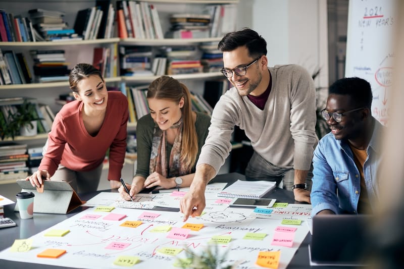 A group of four young professionals engaged in a brainstorming session over a table filled with notes and a laptop.