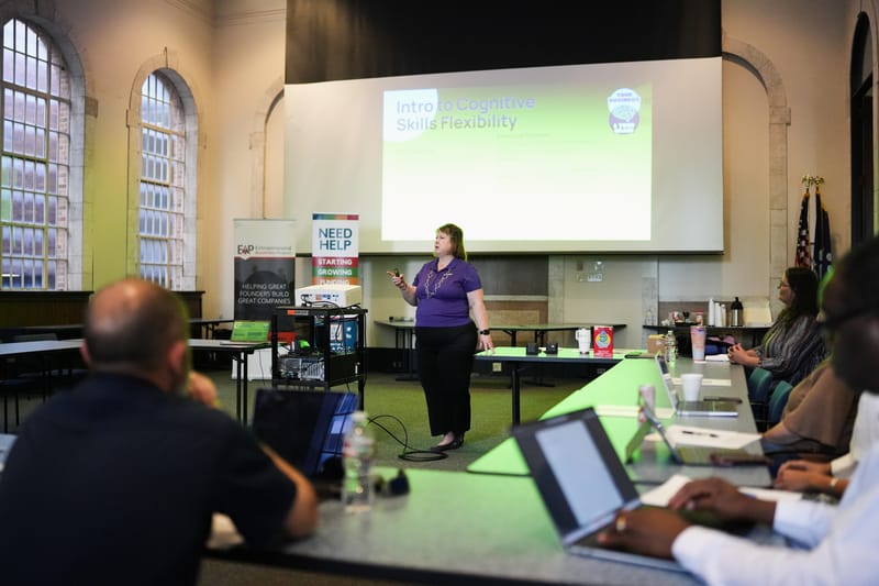 A woman presents a slideshow titled 'Intro to Cognitive Skills Flexibility' to an audience.