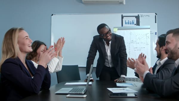 A group of professionals applauding a standing man during a meeting in a conference room.