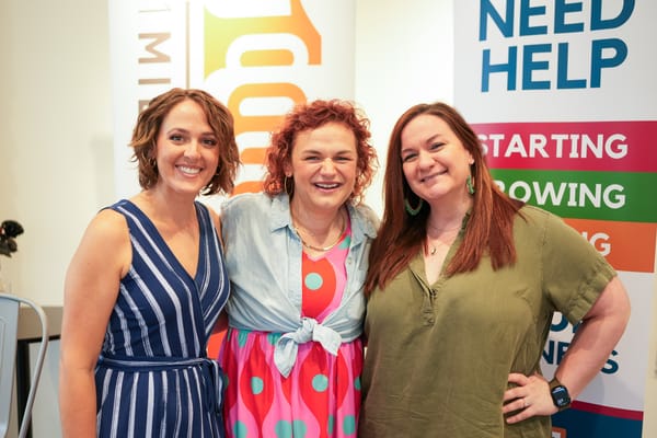 Three women smiling and posing together near event banners.
