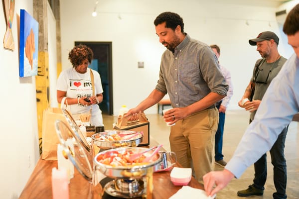 A group of people serving themselves food from a buffet at an art gallery.