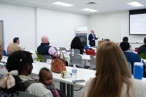 A speaker presents to a seated audience in a classroom setting.